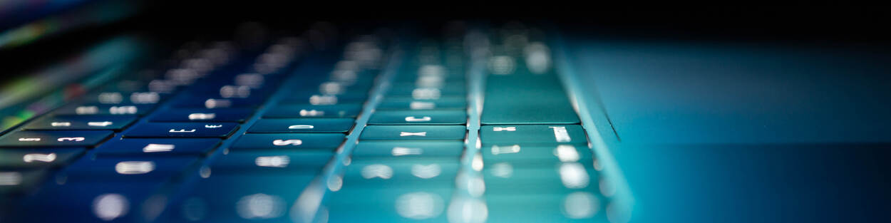 Close-up van een verlicht laptoptoetsenbord in een donkere omgeving, met een blauwe gloed over de toetsen en het touchpad.