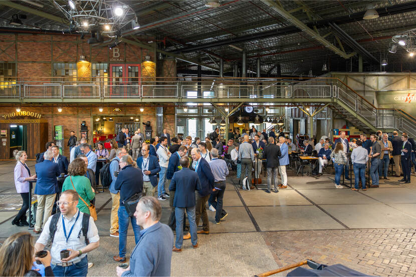Bezoekers van de cyberweerbaarheidsconferentie staan in groepjes te praten tijdens een netwerkpauze in het Spoorwegmuseum.