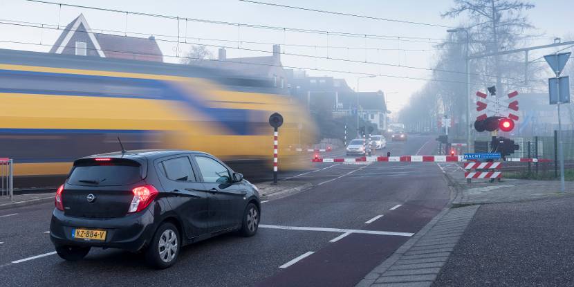 Auto wacht voor slagbomen. Er rijdt een trein voorbij.